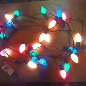 May include: A string of colorful Christmas lights with various colors including red, green, blue, and white. The lights are arranged on a black wire and are lit up, creating a festive display.