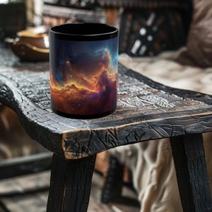 May include: A black coffee mug featuring a vibrant nebula design in shades of orange, blue, and purple. The mug is cylindrical and sits on a dark, textured wooden surface. The mug's interior is black.