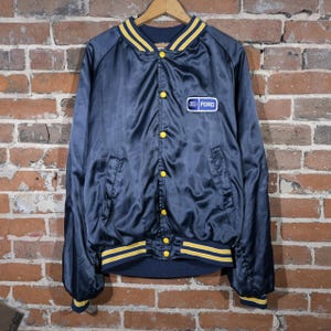 May include: Navy blue satin jacket with yellow stripes on the collar, cuffs, and waist. Features a Ford logo patch on the chest and yellow button closures. A vintage-style bomber jacket.