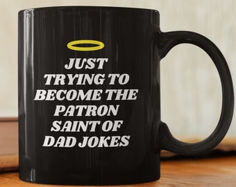 May include: Black coffee mug with a white halo and the text "JUST TRYING TO BECOME THE PATRON SAINT OF DAD JOKES".