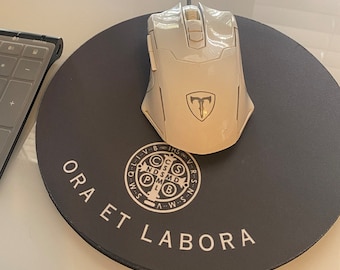 May include: A white wireless mouse with a black logo on a black round mousepad with the text "ORA ET LABORA" and a religious symbol in the center.