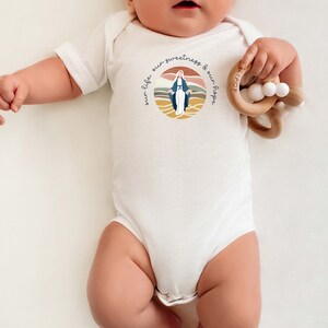Pu&ograve; includere: Body bianco per neonato con un'illustrazione colorata della Vergine Maria e il testo "our life our sweetness & our hope".