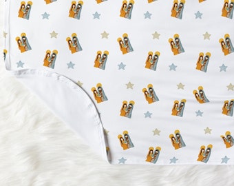 May include: White blanket with a repeating pattern of a nativity scene and stars in shades of yellow, blue, and brown. The blanket is folded over, revealing a white underside.