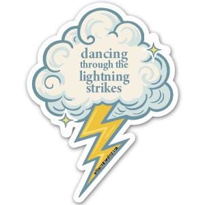 May include: A die-cut sticker featuring a cloud with the text "dancing through the lightning strikes" in a whimsical font. A yellow and blue lightning bolt extends from the cloud, with two small yellow stars. The sticker has a white border.
