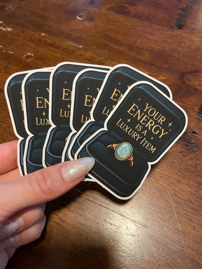May include: A stack of stickers featuring a ring in a jewelry box. The ring has a light blue opal stone and gold band. The text on the sticker reads "YOUR ENERGY IS A LUXURY ITEM."