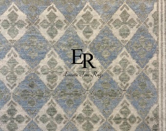 May include: A rectangular rug with a repeating diamond pattern in shades of blue, gray, and white. The design features floral-like motifs within the diamonds. The rug has a textured appearance and the text "Exceotic Fine Rugs" is visible.