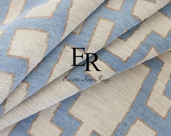 May include: Close-up of a folded rug with a geometric pattern. The rug features a light blue and beige zig-zag design. The text "ER Exotic Fine Rugs" is visible in the image.