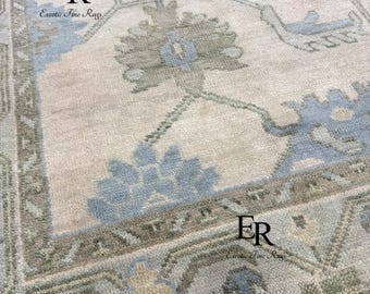 Könnte beinhalten: Nahaufnahme eines beige-blauen Teppichs mit Muster. Der Teppich weist ein zentrales Blumendesign in Grün- und Blautönen auf, umgeben von einem Rand mit geometrischen Mustern. Der Text "ER Exotic Fine Rugs" ist an zwei Stellen sichtbar.