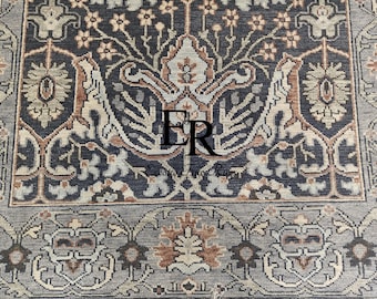 Puede incluir: Un primer plano de una alfombra azul oscuro con un patrón floral. La alfombra tiene un borde marrón claro y un medallón central con las letras "ER" en el centro. La alfombra está hecha de lana y tiene una construcción anudada a mano.