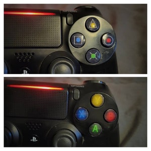 May include: A black PlayStation 4 controller with a red light bar and colorful face buttons. The buttons are labeled with the symbols: triangle, square, circle, cross, X, Y, and A.
