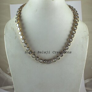 May include: A gold necklace with a row of round, clear diamonds set in black metal. The necklace is on a white mannequin bust. "Shree Balaji Creations" is written on the bust.
