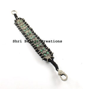 May include: A black cord bracelet with silver and green gemstone accents. The bracelet has a clasp closure and features a repeating pattern of silver and green gemstones.
