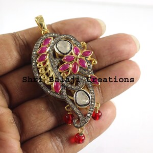 May include: A gold pendant with a floral design featuring pink gemstones and white diamonds. The pendant is set in a silver frame and has a dangling chain with red beads.