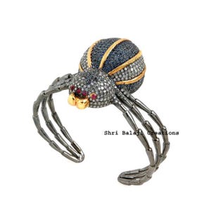Könnte beinhalten: Ein einzigartiges Armband in Spinnenform. Der Körper der Spinne ist eine Mischung aus Dunkelblau und Silber, mit goldenen Akzenten. Die Beine sind dunkelgrau. Die Augen der Spinne sind rot. Der Text "Shri Balaji Creations" ist sichtbar.