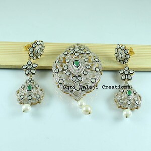 May include: A jewelry set featuring a central pendant and two matching drop earrings. Each piece is crafted with silver-toned metal, inlaid with numerous small clear stones, a central green stone, and a single white pearl drop at the base.