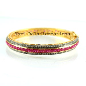 Puede incluir: Un brazalete de oro con una fila de piedras preciosas cuadradas de color rosa y una fila de piedras preciosas más pequeñas y transparentes. El brazalete está inscrito con el texto "Shri Balajicreations".