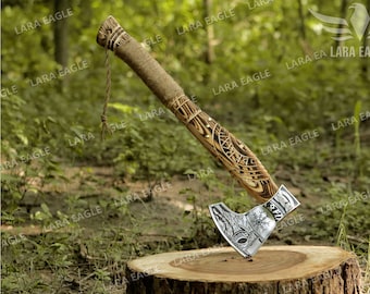 May include: A silver axe with a wooden handle. The handle is decorated with a carved design and the axe head has a Viking-inspired design. The axe is resting on a wooden stump.