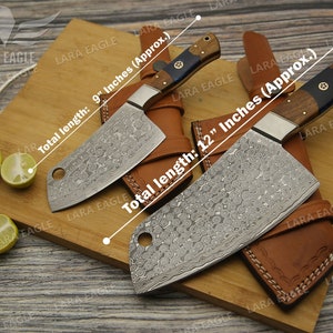May include: Two cleavers with leather sheaths on a wooden cutting board. The cleavers have a hammered finish and wooden handles. The cleavers are 9 inches and 12 inches long.