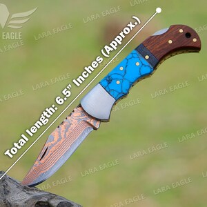 Op de afbeelding: Een vouwmes met een turquoise en koperkleurig gepatenteerd blad en een bruin houten handvat. Het mes is 16,5 cm lang.