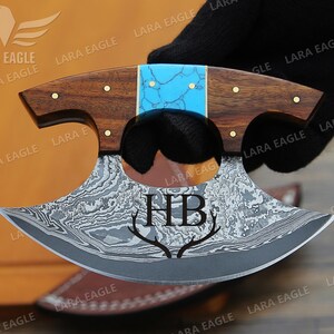 May include: A personalized, hand-forged, Damascus steel knife with a turquoise and wood handle. The blade is engraved with the initials "HB" and a pair of antlers.
