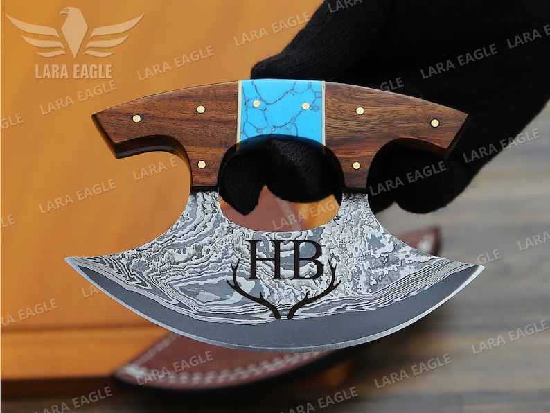 May include: A personalized, hand-forged, Damascus steel knife with a turquoise and wood handle. The blade is engraved with the initials "HB" and a pair of antlers.