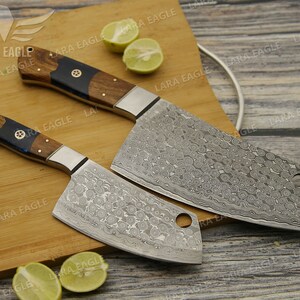 May include: Two kitchen knives with wooden handles and a patterned steel blade. The knives are on a wooden cutting board with lemons.