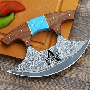 May include: A personalized cleaver with a blue and brown handle. The blade is made of Damascus steel and has a decorative pattern. The cleaver is engraved with the name "ARTHER".