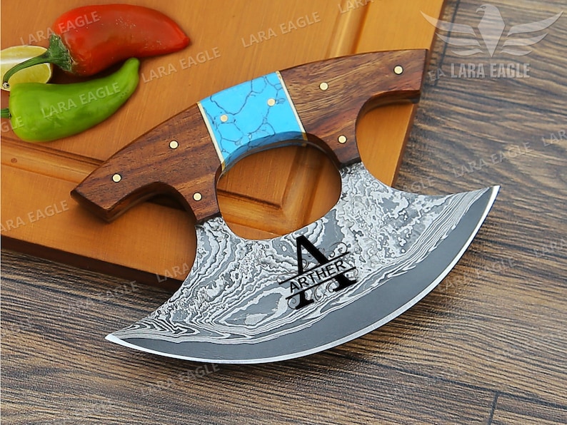 May include: A personalized cleaver with a blue and brown handle. The blade is made of Damascus steel and has a decorative pattern. The cleaver is engraved with the name "ARTHER".