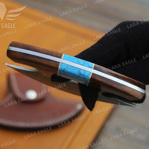 May include: A brown and silver folding knife with a turquoise inlay. The knife has a leather sheath.