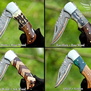 May include: Four folding knives with different handle designs. The blades have a patterned design with a copper-colored edge. The handles are made of wood, stag horn, and green material. Text on the image reads "Stag Horn + Rose Wood", "Ram Horn + Rose Wood", "Rose Wood + Ash Wood", and "Olive + Green".