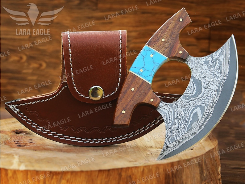 May include: A handmade Damascus steel cleaver with a turquoise and wood handle. The cleaver is in a brown leather sheath.