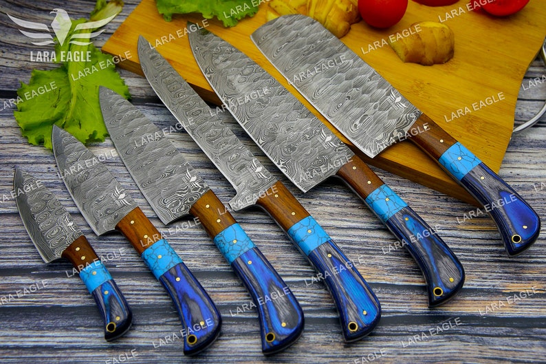 May include: Set of five kitchen knives with blue and turquoise handles. The knives have a Damascus steel blade pattern and are arranged on a wooden surface.