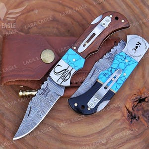 May include: Two personalized pocket knives with turquoise inlays and Damascus steel blades. One knife has the name "Smith" engraved on it, and the other has the initials "K.C." engraved on it.
