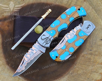 May include: A set of custom knives with wooden handles inlaid with blue accents. The blades have a patterned design. Includes a sharpening steel and a leather case. The knife is engraved with the name "SMITH".