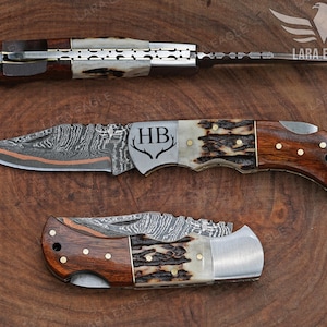 May include: Three folding knives with intricate blade patterns and wooden handles are displayed on a wooden surface. The knives have a mix of brown, white, and silver tones. One knife is fully extended, while the others are partially open, showcasing the detailed craftsmanship.