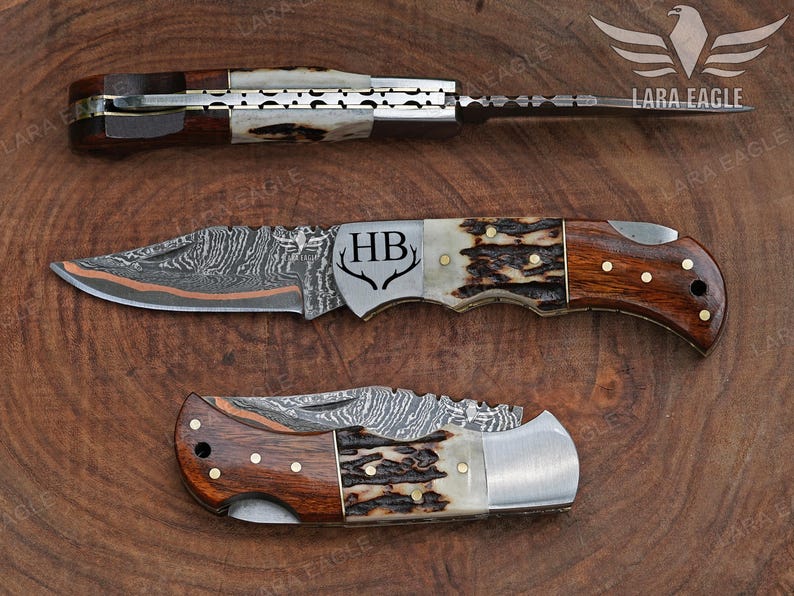 May include: Three folding knives with intricate blade patterns and wooden handles are displayed on a wooden surface. The knives have a mix of brown, white, and silver tones. One knife is fully extended, while the others are partially open, showcasing the detailed craftsmanship.