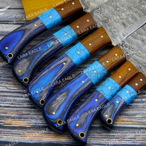 May include: A set of six kitchen knives with blue and brown handles. The blades are made of Damascus steel and have a wavy pattern. The handles are made of wood and have a blue and turquoise inlay.