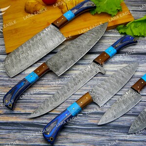 May include: Five kitchen knives with blue and brown handles and a patterned steel blade. The knives are arranged on a wooden surface.