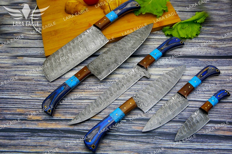 May include: Five kitchen knives with blue and brown handles and a patterned steel blade. The knives are arranged on a wooden surface.