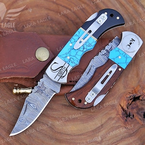 May include: A personalized pocket knife with a turquoise and black handle. The blade is Damascus steel with a decorative pattern. The knife is engraved with the initials "S" and "K" and the name "Smith".