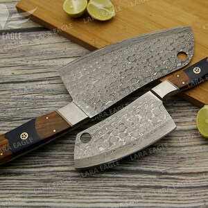 May include: Two stainless steel cleavers with wooden handles. The cleavers have a hammered finish and a decorative pattern. The handles are brown with black accents.
