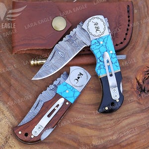 May include: Two personalized pocket knives with turquoise inlays and Damascus steel blades. The knives have personalized engravings that read "ABC" and "K&C".