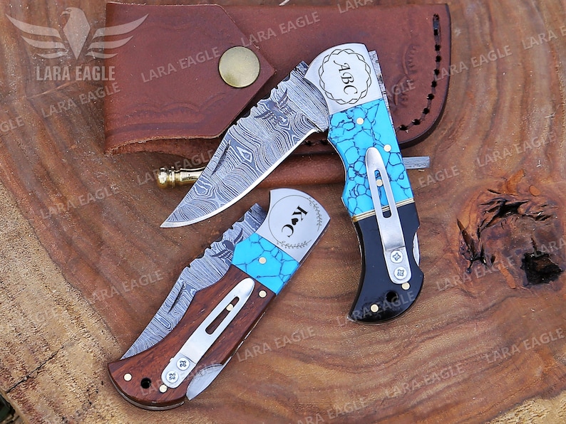 May include: Two personalized pocket knives with turquoise inlays and Damascus steel blades. The knives have personalized engravings that read "ABC" and "K&C".