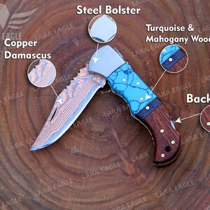 Op de afbeelding: Een vouwzakmes met een koperen Damascus stalen lemmet, een handvat van turquoise en mahoniehout en een stalen bolster. Het mes heeft een rugvergrendeling.