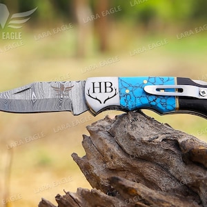May include: A pocket knife with a blue and black handle, a stainless steel blade, and the initials "HB" engraved on the handle. The blade is partially open, revealing a damascus pattern.