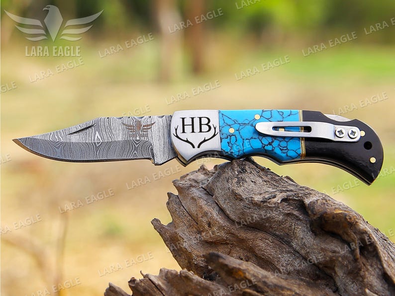 May include: A pocket knife with a blue and black handle, a stainless steel blade, and the initials "HB" engraved on the handle. The blade is partially open, revealing a damascus pattern.