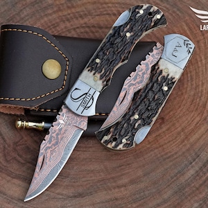 May include: A set of three knives with brown and tan handles, a copper-colored blade, and a brown leather case. The knives have the initials "S" and "A&J" engraved on them. The blades have a unique pattern.