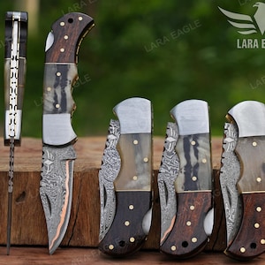 May include: A collection of folding knives with intricate designs. The knives feature wooden handles, metal blades, and decorative accents. The blades have a unique pattern, and the handles have a mix of dark and light wood. The image includes the text "LARA EAGLE".