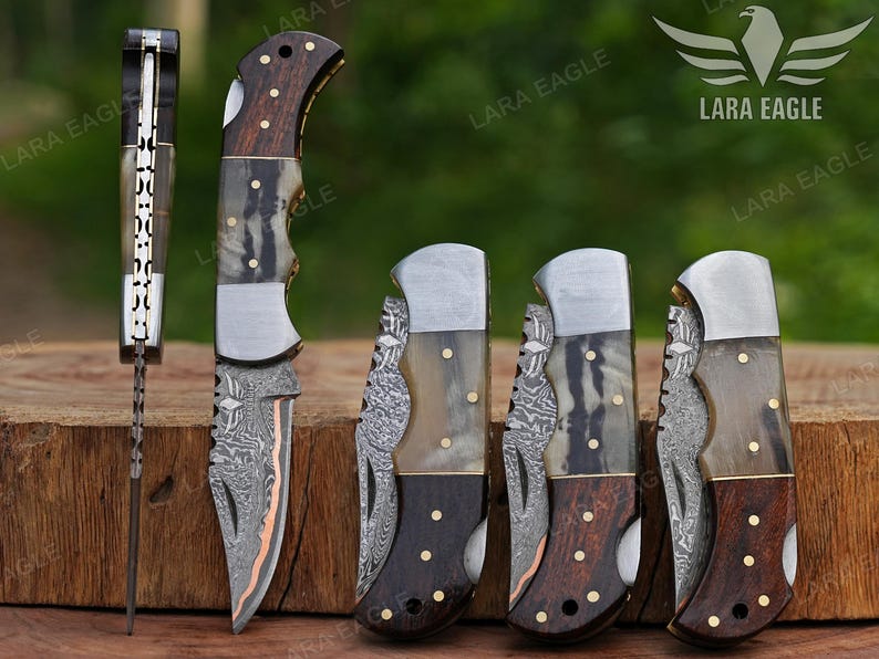 May include: A collection of folding knives with intricate designs. The knives feature wooden handles, metal blades, and decorative accents. The blades have a unique pattern, and the handles have a mix of dark and light wood. The image includes the text "LARA EAGLE".