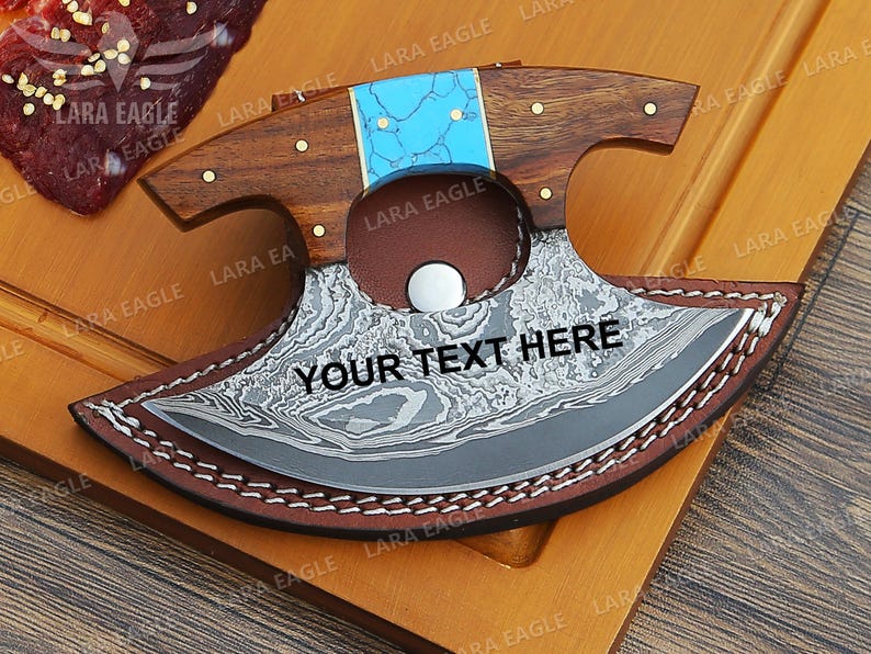 May include: A personalized, curved, stainless steel knife with a wooden handle and a turquoise inlay. The knife is in a brown leather sheath with decorative stitching. The knife is engraved with the text "YOUR TEXT HERE".